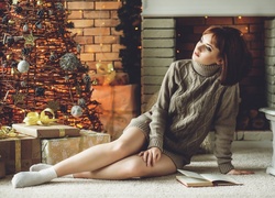 Zamyślona kobieta w swetrze przy kominku i świątecznej choince