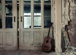 Zaniedbane pomieszczenie z gitarą opartą o przeszklone drzwi
