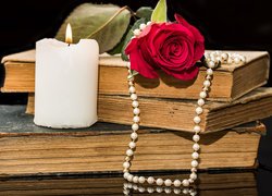 Zapalona świeca i róża z perłami na książkach