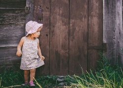 Zapatrzona dziewczynka w letniej sukience przy drewnianych drzwiach