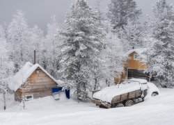 Zasypany śniegiem samochód obok domów pod drzewami