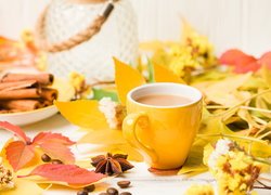 Żółty kubek z kawą pośród jesiennych liści
